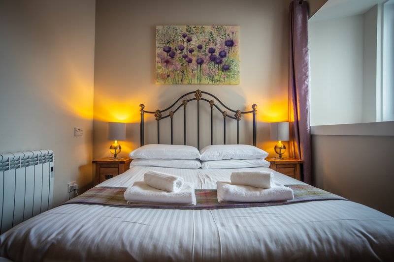 Bedroom with metal-frame bed, white bedding, folded towels, and bedside lamps