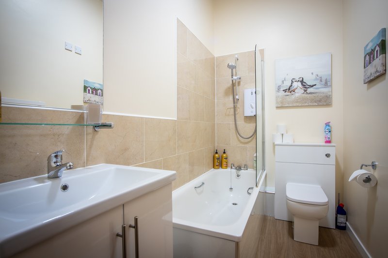 Modern bathroom with white sink, bathtub with shower screen, toilet and wooden flooring