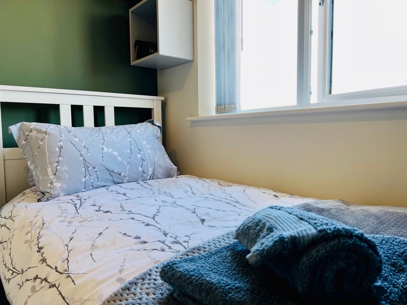Bedroom with single bed, blue patterned bedding, pillows, and folded towel on bed