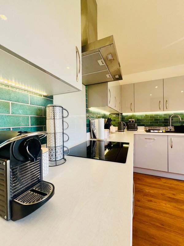 Modern kitchen with white countertops, turquoise subway tiles, coffee machine, and wooden flooring