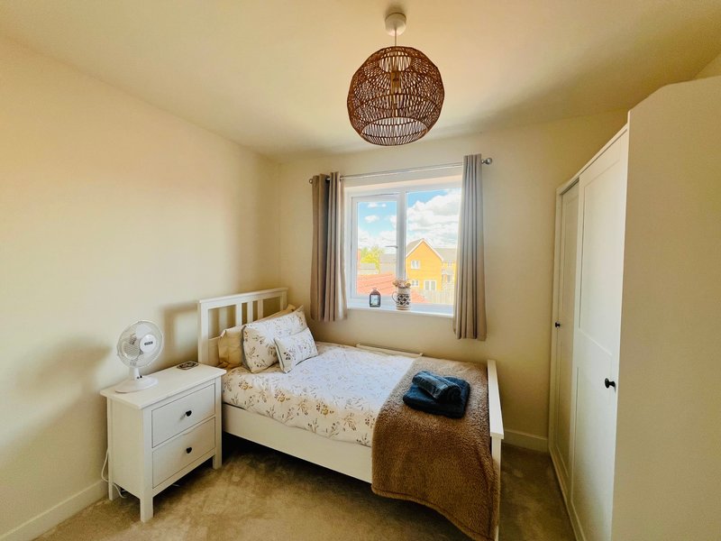 Bedroom with single bed, white nightstand, woven pendant light and window with curtains