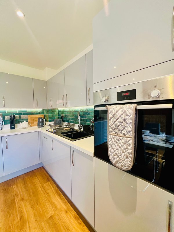 Modern kitchen with white cabinetry, green tile backsplash, black appliances and wooden flooring