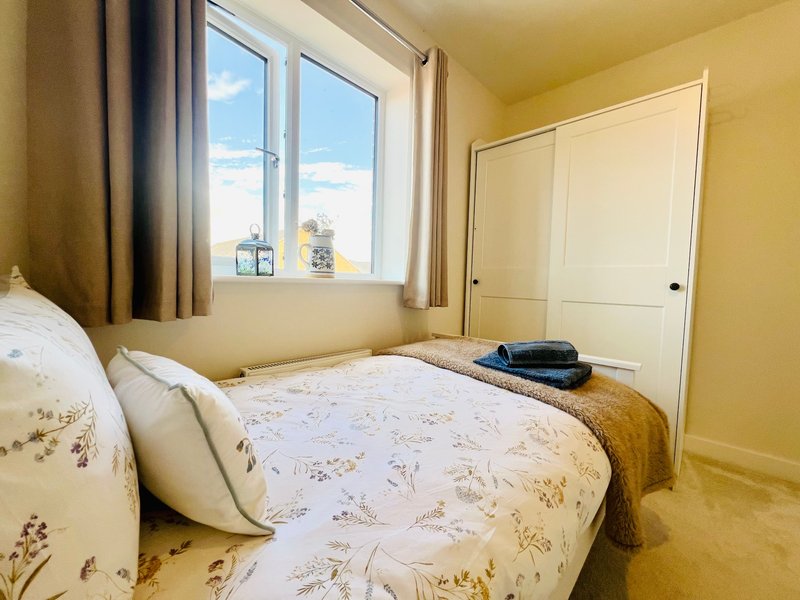 Bright bedroom with double bed, patterned bedding, large window with sea view, and cream sliding wardrobe