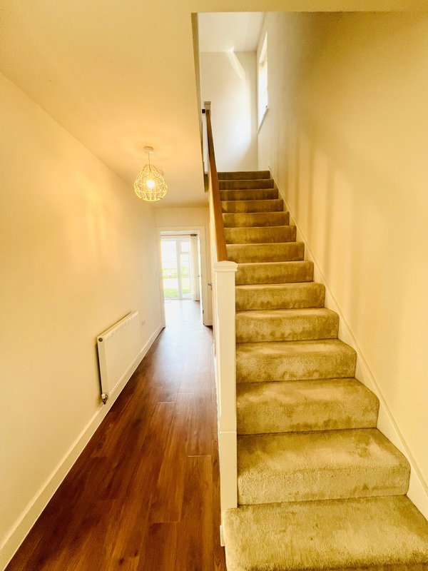 Hallway with wooden floor, yellow walls, staircase with beige carpet and pendant light