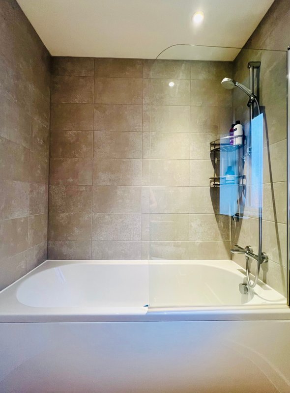 Modern bathroom with white bathtub, brown tile walls, and glass shower enclosure