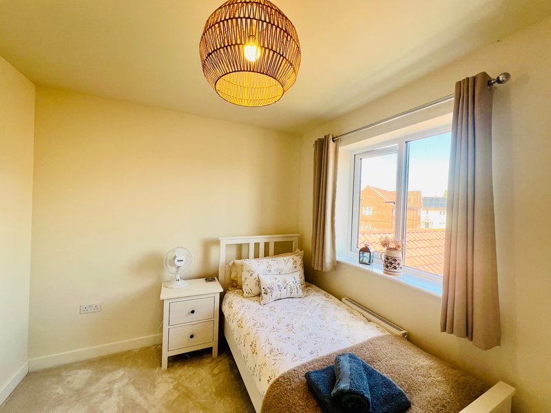 Bright bedroom with single bed, white nightstand, woven ceiling lamp, and window with city view