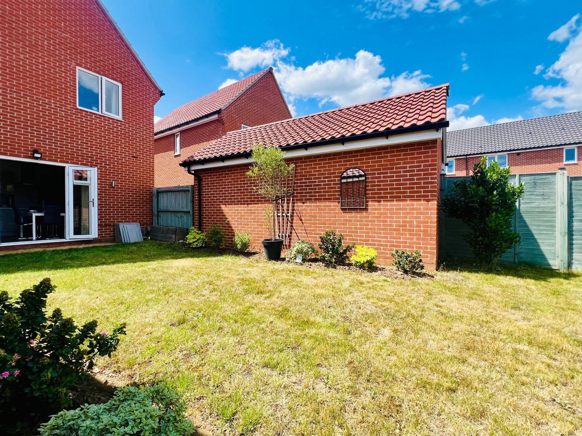 Brick residential property with garden, garage and lawn area on sunny day