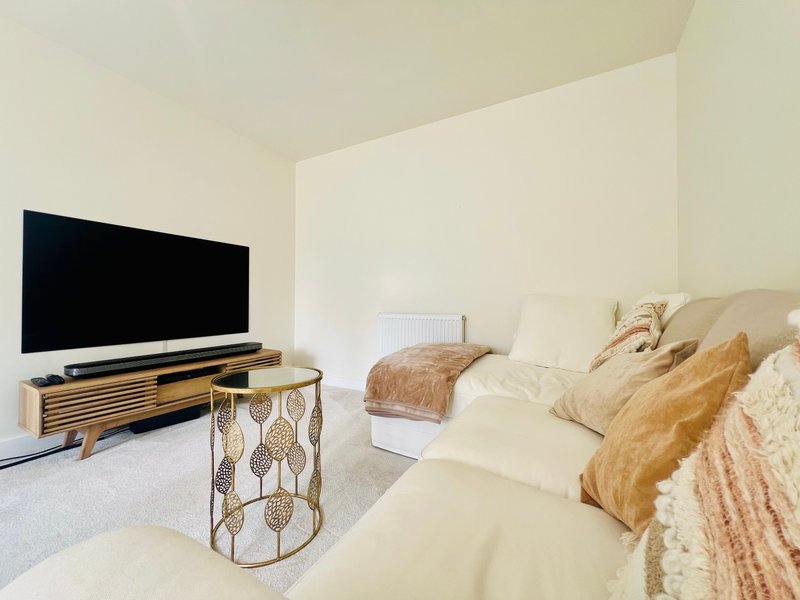 Modern bedroom with two beds, TV on wooden stand, and neutral beige decor