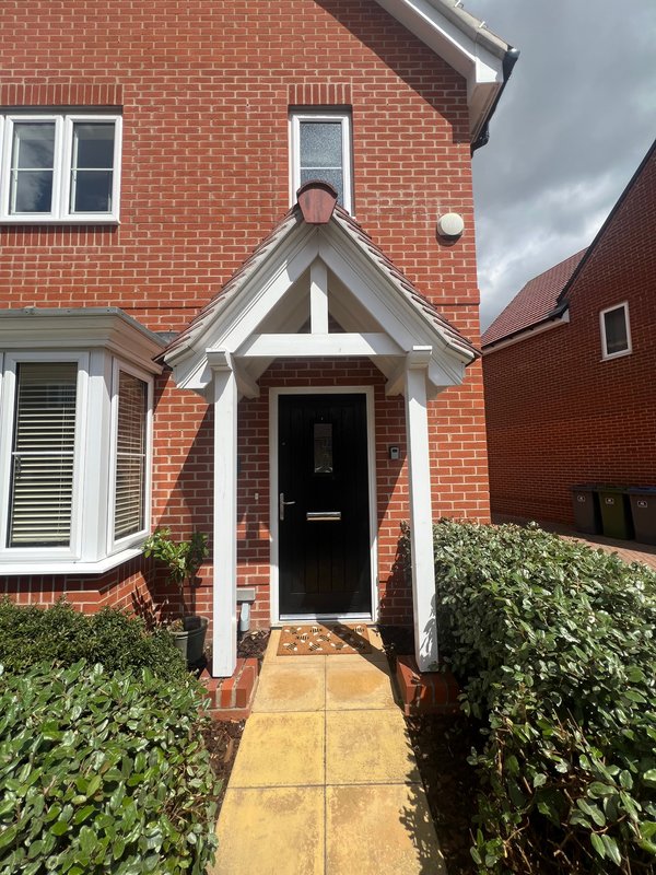 Red brick house exterior with white-framed entrance porch, black door, and front pathway