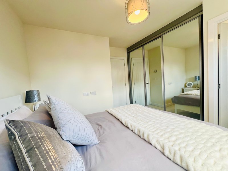 Bright bedroom with double bed, patterned pillows, built-in mirrored wardrobe and ceiling light