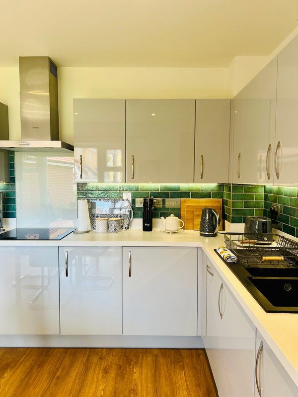 Modern kitchen with white cabinets, green tile splashback, yellow countertop, and wooden flooring