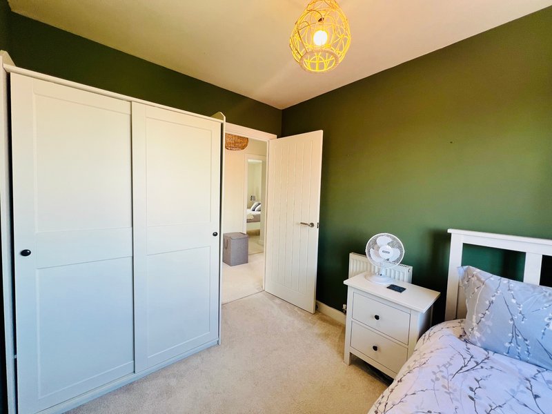 Bedroom with green accent wall, white wardrobe, bedside table, and pendant light fixture
