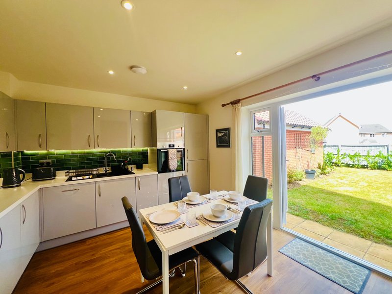 Modern kitchen and dining area with white cabinets, green tile backsplash, dining table, and garden view