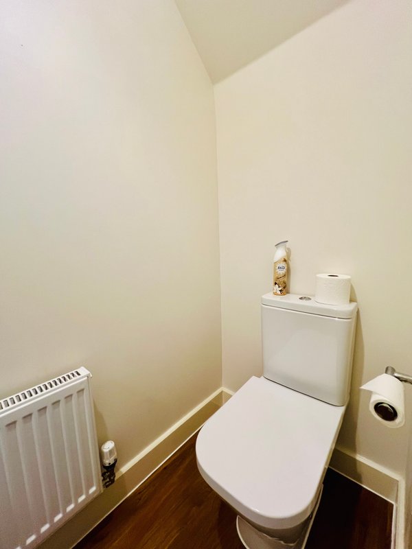 Small bathroom with white toilet, radiator, and washing machine against cream walls