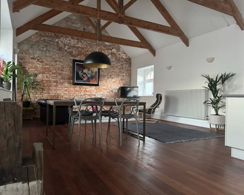 Open-plan living space with exposed wooden beams, brick wall, dining table and chairs