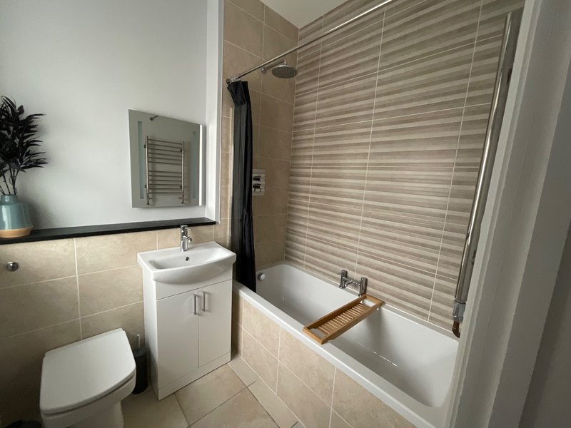Modern bathroom with toilet, white vanity sink, bathtub with shower enclosure and venetian blinds