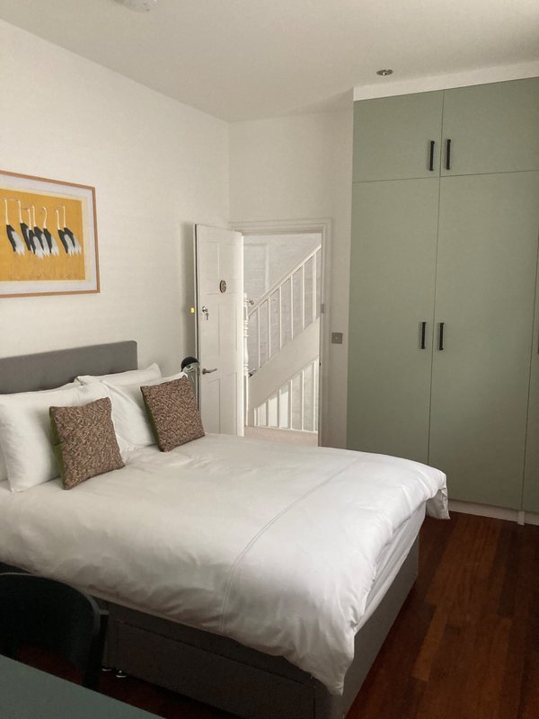 Modern bedroom with double bed, white bedding, sage-green fitted wardrobes and wooden floor