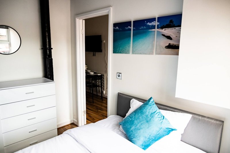 Modern bedroom with double bed, turquoise cushion, white dresser and beach artwork