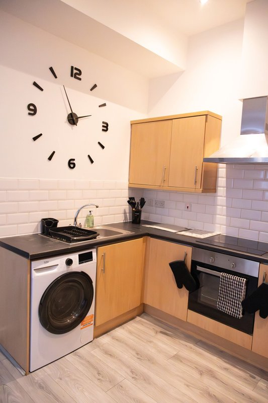 Kitchen with wooden cabinets, black countertop, washing machine, wall clock and white subway tile backsplash
