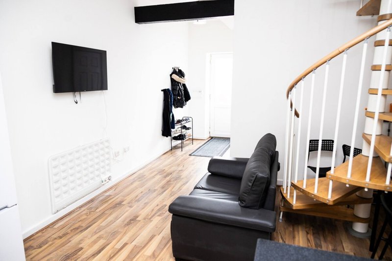 Open-plan living area with black leather armchair, wooden flooring, stairs, and wall-mounted TV