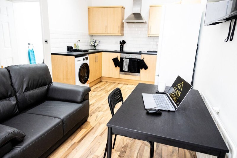 Open-plan living space with black leather sofa, dining table, kitchen with wooden cabinets and appliances