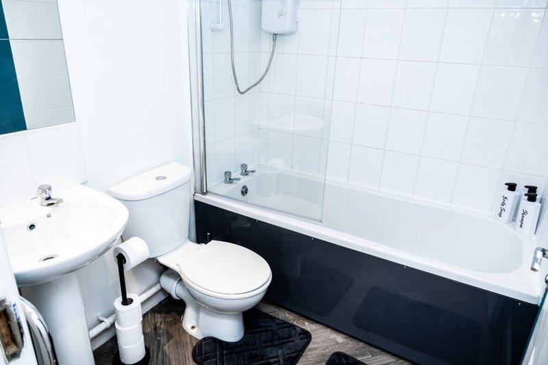 Modern bathroom with white tiles, toilet, sink, bathtub with glass shower screen