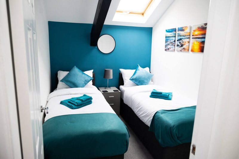 Modern bedroom with twin beds, teal headboard, white bedding and teal accents