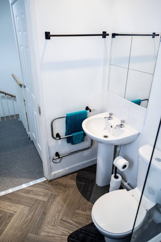 Compact bathroom with pedestal sink, toilet, shower enclosure and herringbone floor