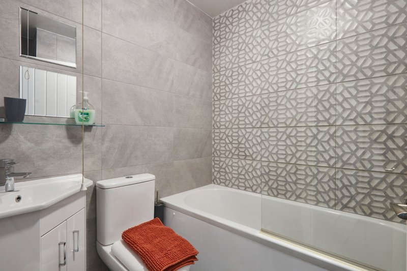 Modern bathroom with vanity, toilet, bathtub, patterned tile wall and mirror