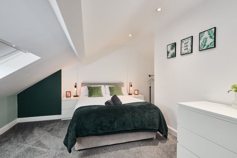 Attic bedroom with double bed, dark green accent wall, white storage, and framed botanical prints