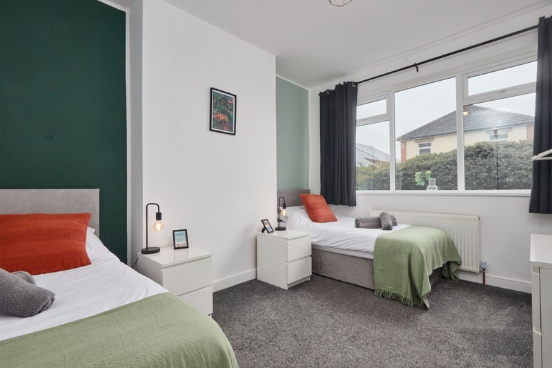 Bright bedroom with two single beds, green feature wall, white bedside table and large window