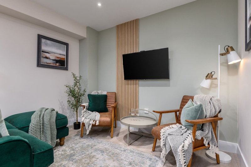Modern living room with green velvet sofa, wooden chairs, wall-mounted TV and decorative cushions