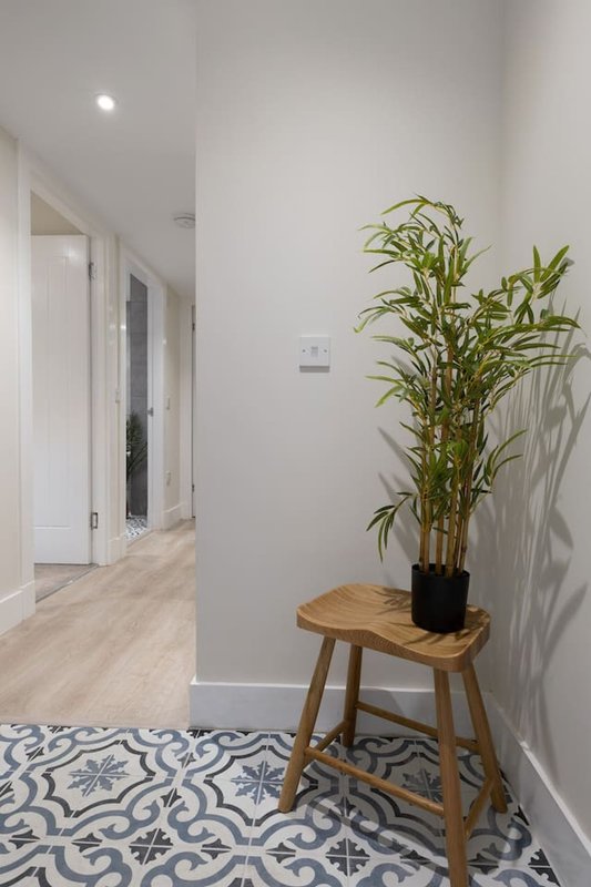 Bright hallway with wooden stool, potted plant, patterned floor tiles and white walls