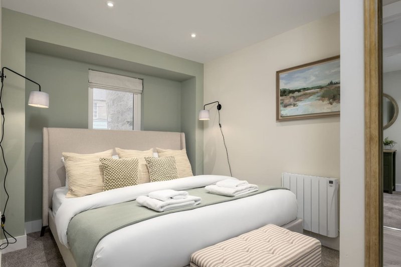 Modern bedroom with double bed, green headboard wall, pendant lamps and framed landscape art