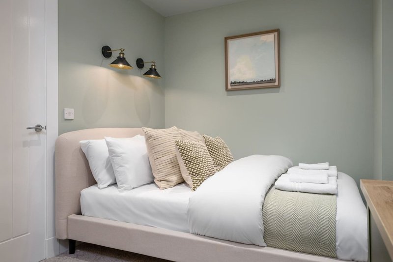 Bedroom with upholstered bed, white bedding, decorative pillows and throw blanket, wall sconces and framed artwork