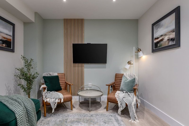 Modern living room with two wooden armchairs, wall-mounted TV, coffee table and green accents