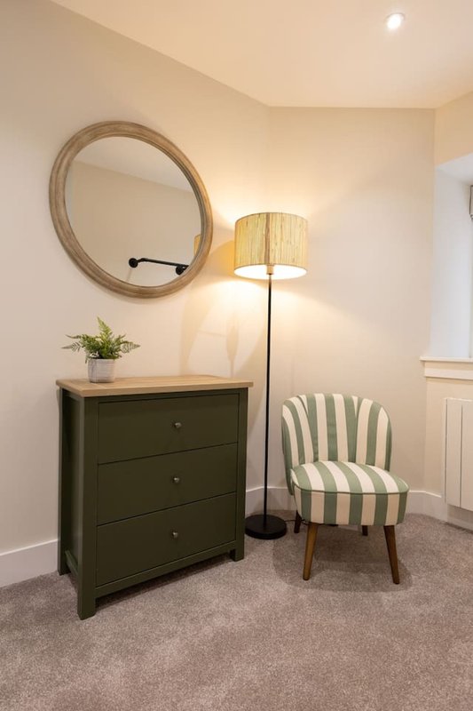 Bedroom corner with green chest of drawers, round mirror, striped accent chair and floor lamp