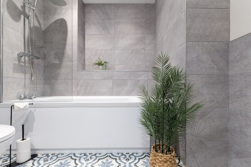 Modern bathroom with bathtub, grey tile walls, potted plant and patterned floor