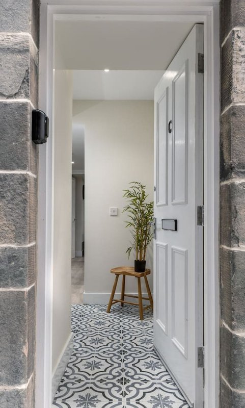 Modern hallway with patterned tile floor, white doors, potted plant on wooden stool