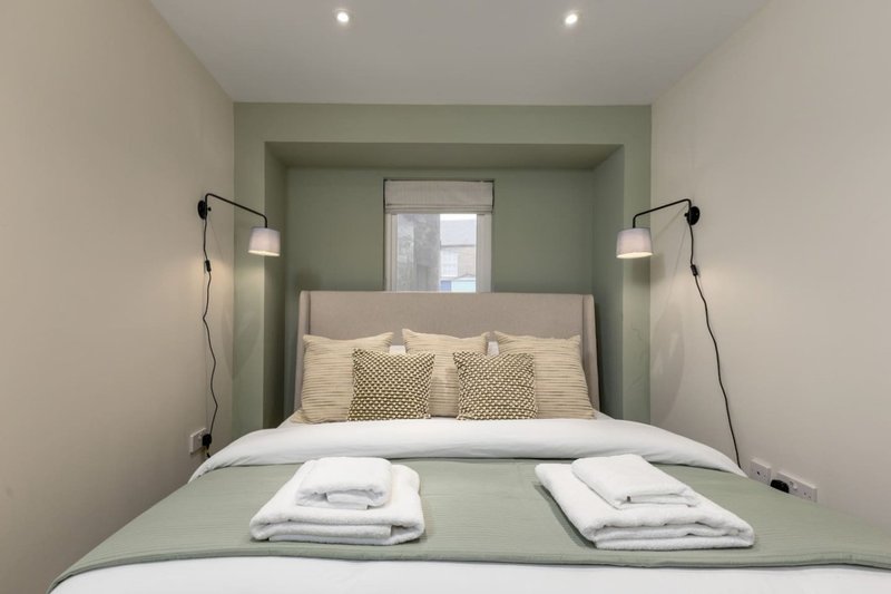 Modern bedroom with double bed, green accent wall, pendant lamps, and folded towels