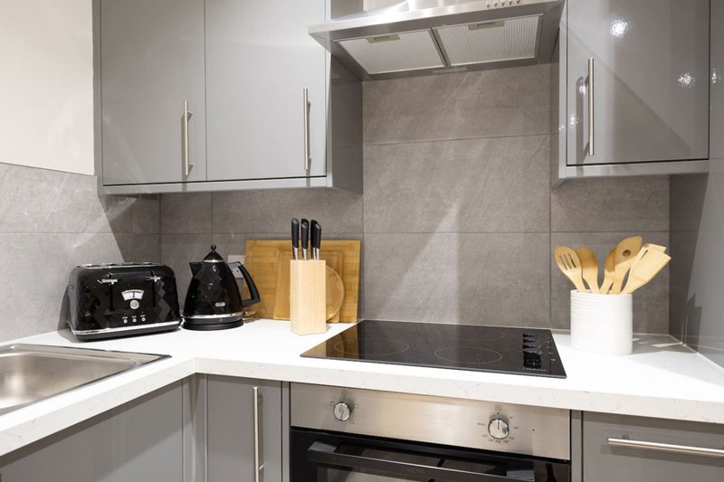 Modern kitchen with grey cabinets, white countertop, black appliances and utensil holders