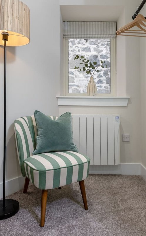 Modern bedroom corner with striped green and white armchair, floor lamp, and window with plant