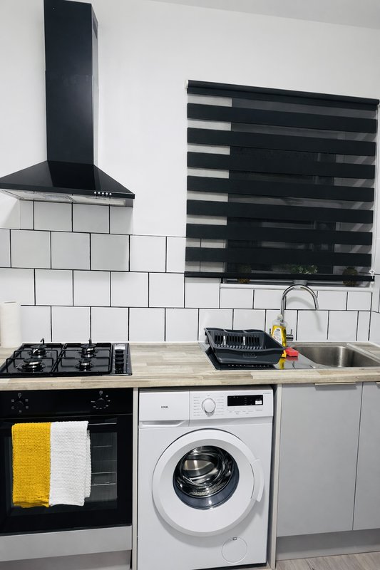Modern kitchen with white subway tiles, gas hob, integrated washing machine, and black range hood