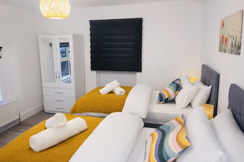 Bright modern bedroom with two single beds, yellow bedding, storage wardrobe and pendant light