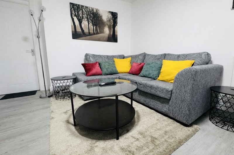 Modern living room with gray corner sofa, colorful cushions, round black coffee table, white rug
