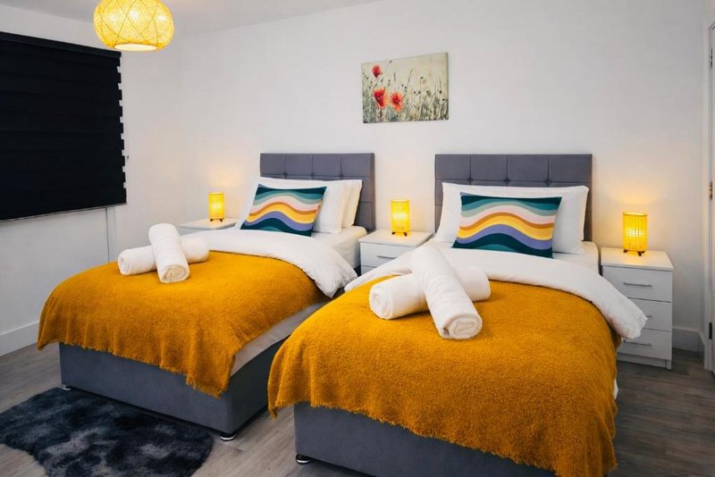 Twin bedroom with two beds, orange blankets, white pillows, yellow lamps, and wall art