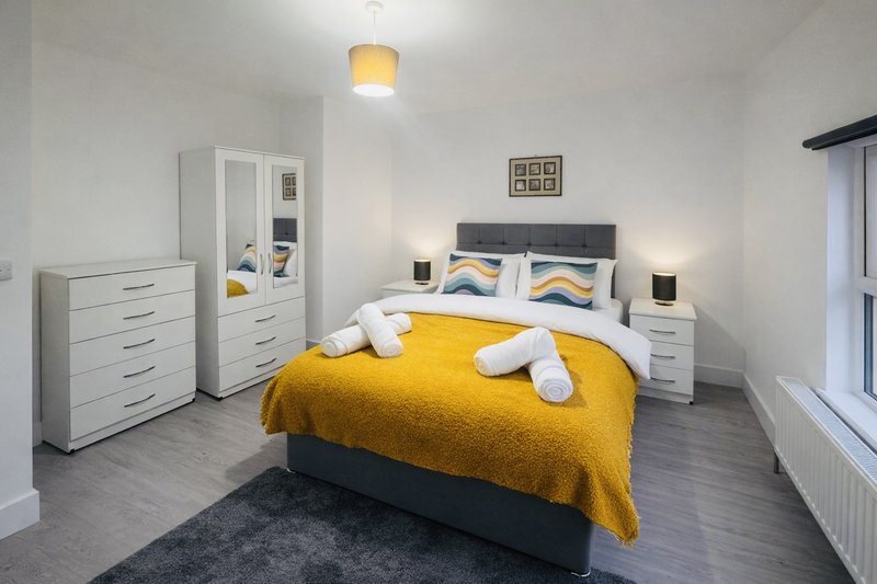 Modern bedroom with double bed, yellow bedding, white furniture, and pendant ceiling light