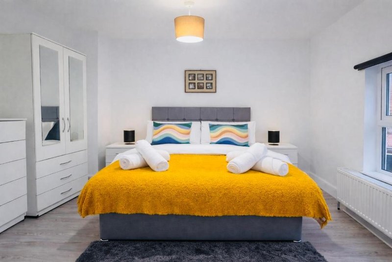 Bright modern bedroom with double bed, yellow bedding, white wardrobes and pendant ceiling light
