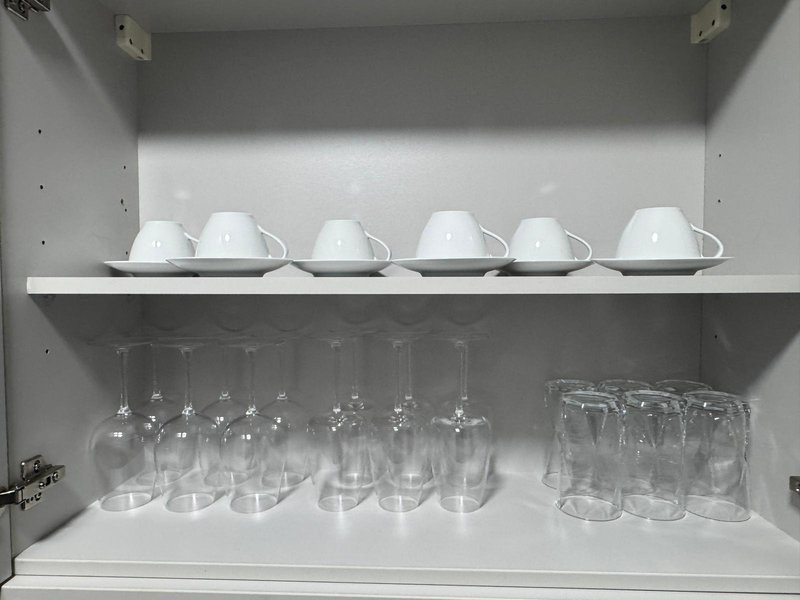 White kitchen cabinet shelf with white bowls and clear drinking glasses neatly arranged