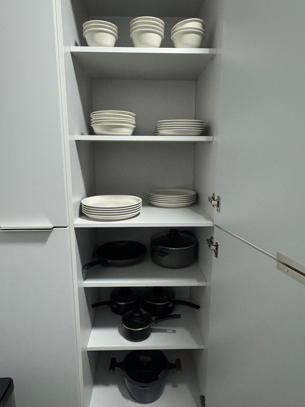 White kitchen cabinet interior with shelves displaying stacked plates and black cookware